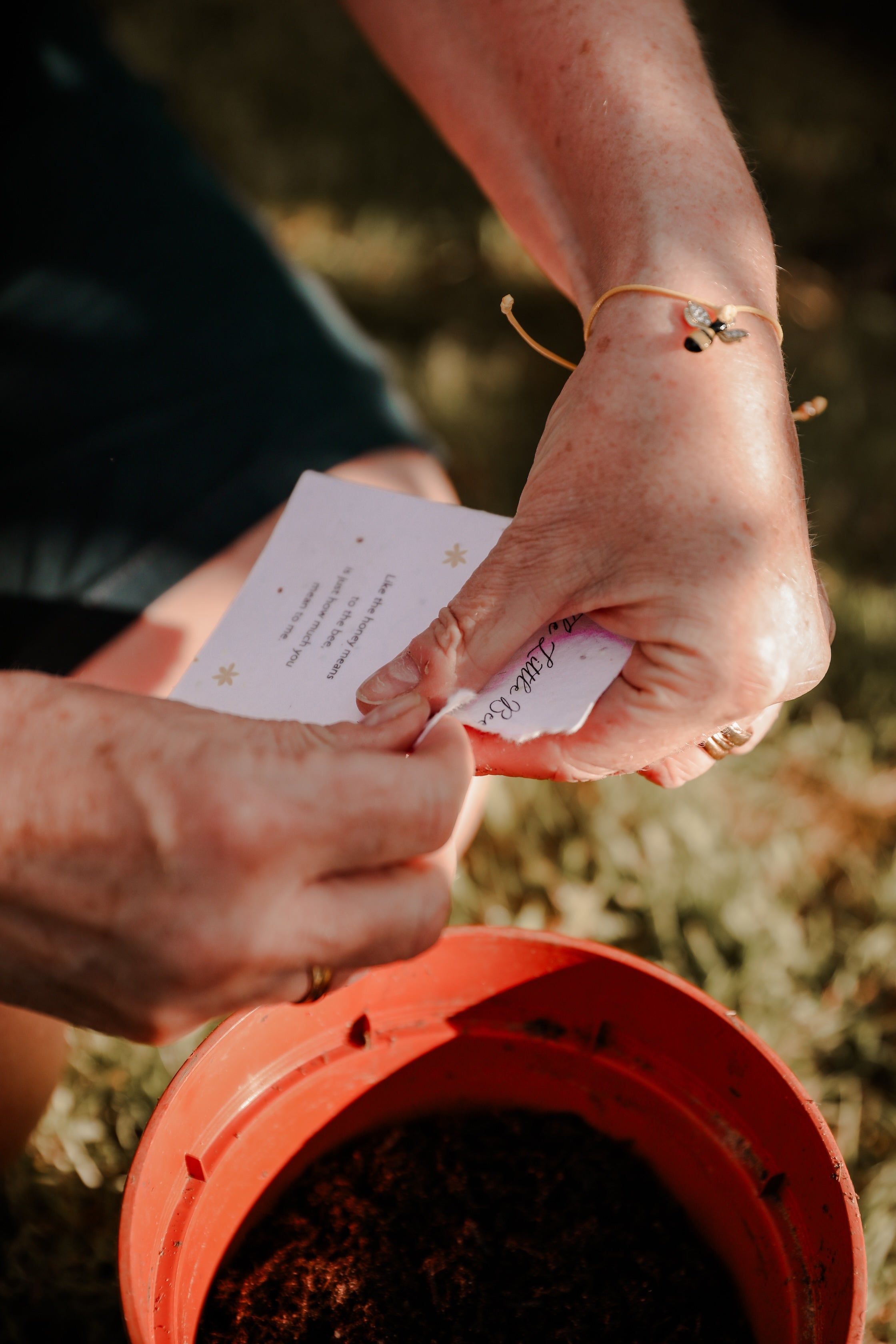 A woman's hands tearing an eco-friendly poem card ready to plant, wearing a cute friendship bracelet