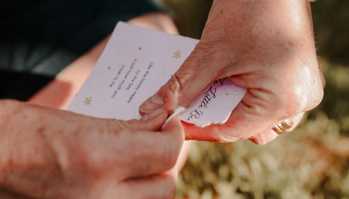 A woman's hands tearing an eco-friendly poem card ready to plant, wearing a cute friendship bracelet