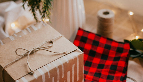 A white jar with fir branches and a brown wrapped gift on tartan fabric