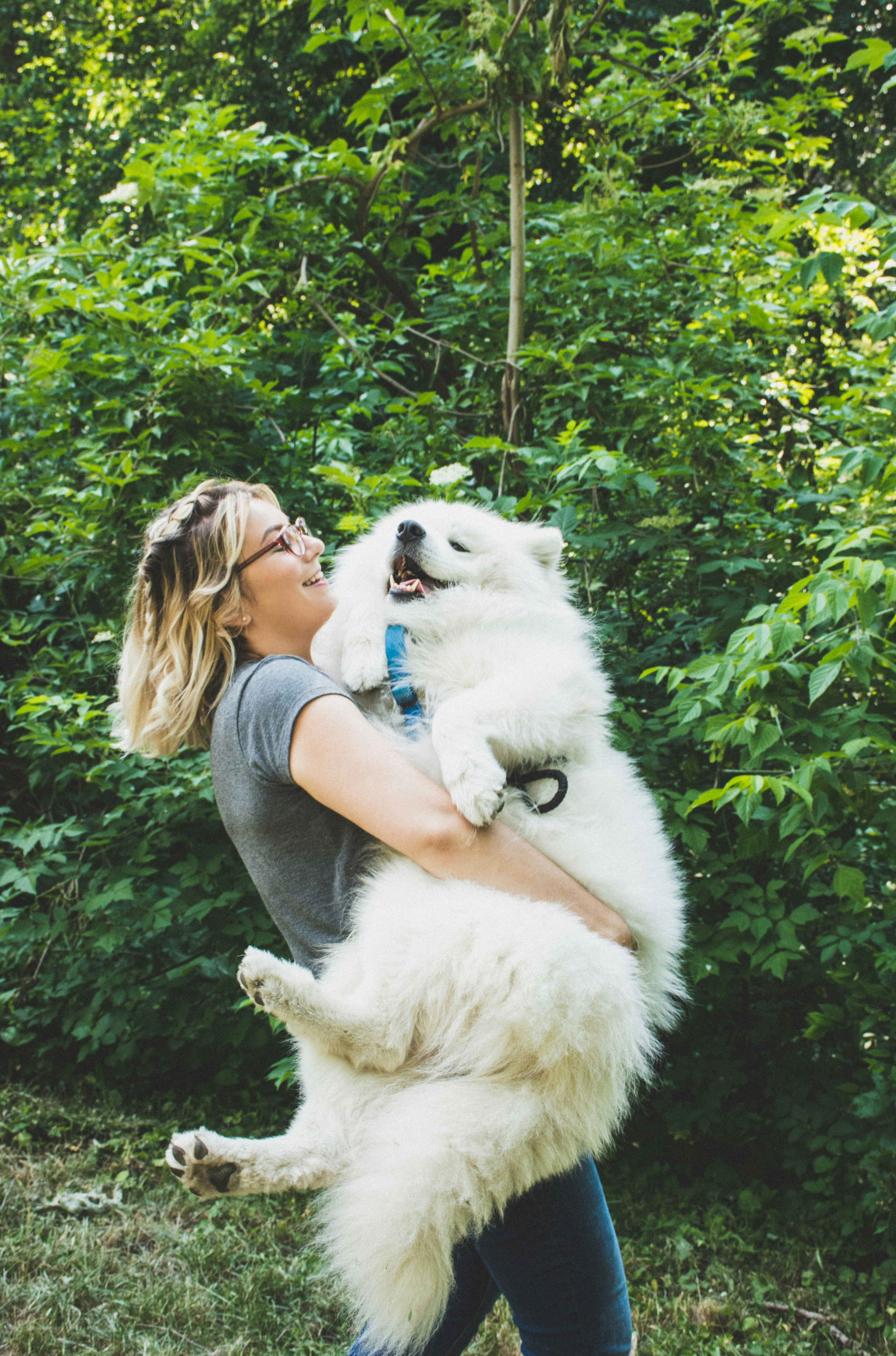 A woman cuddling a big fluffy white dog in a forest