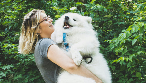 A woman cuddling a big fluffy white dog in a forest