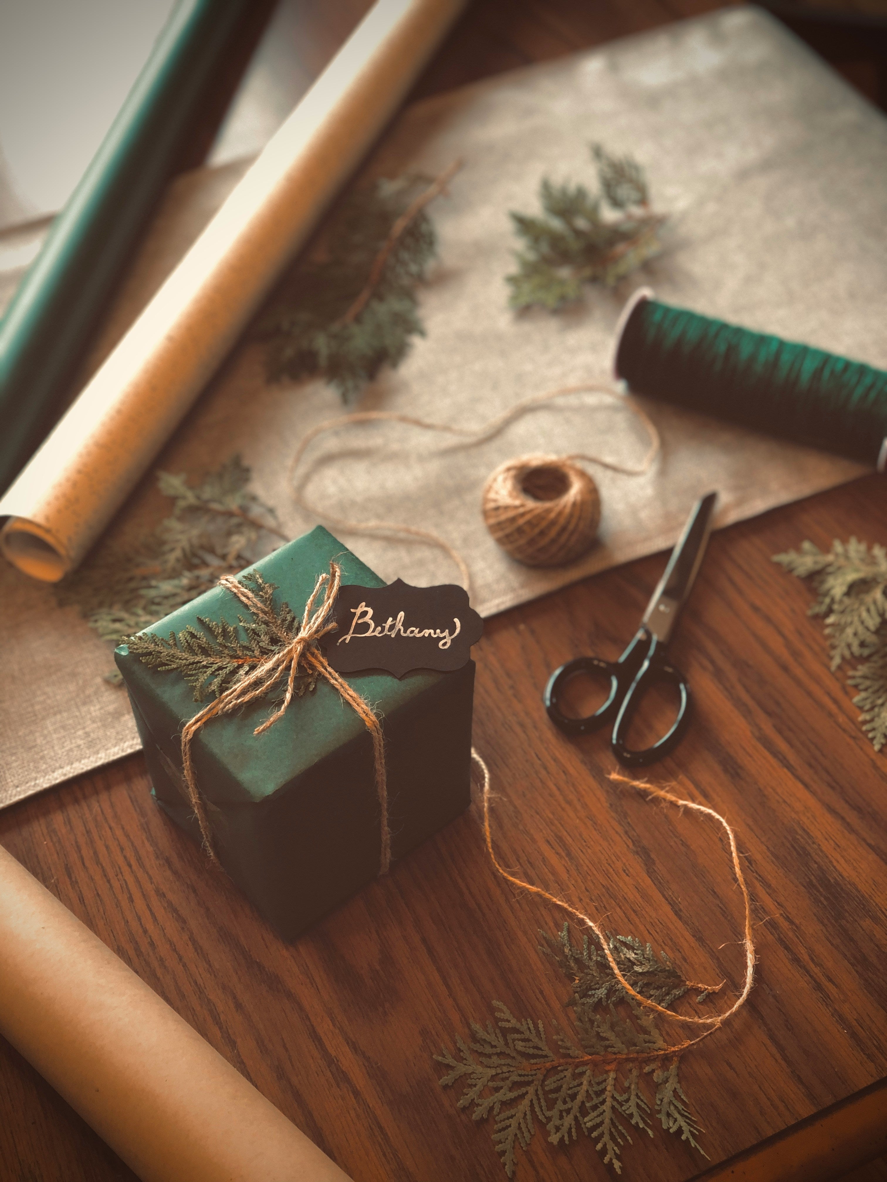 A wooden table with a neatly wrapped green box tied up with string, with a Secret Santa label on the package