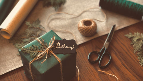 A wooden table with a neatly wrapped green box tied up with string, with a Secret Santa label on the package