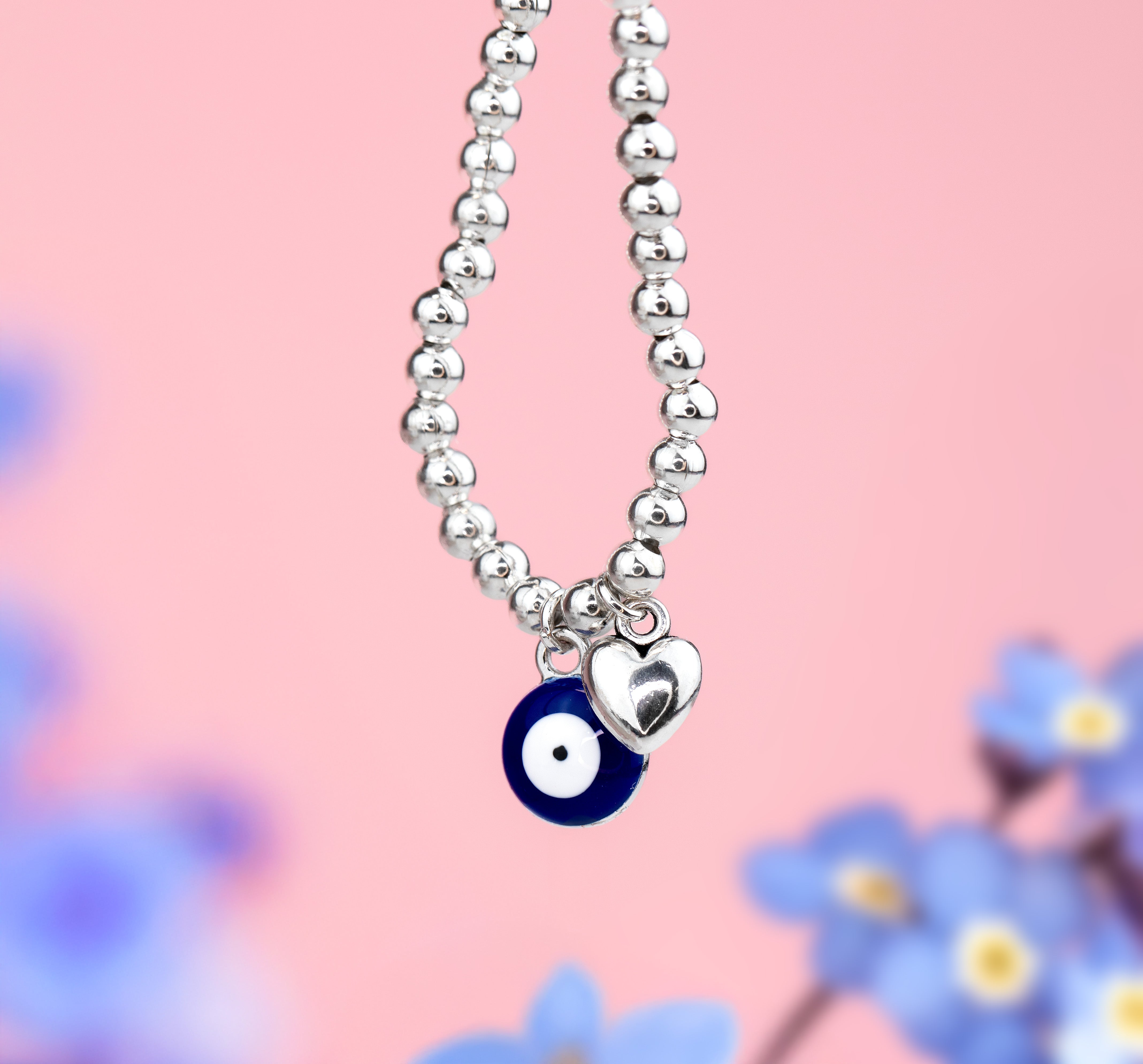 Pink background with evil eye charm bracelet and a little heart charm bracelet on a silver beaded bracelet, a perfect good luck gift under £20