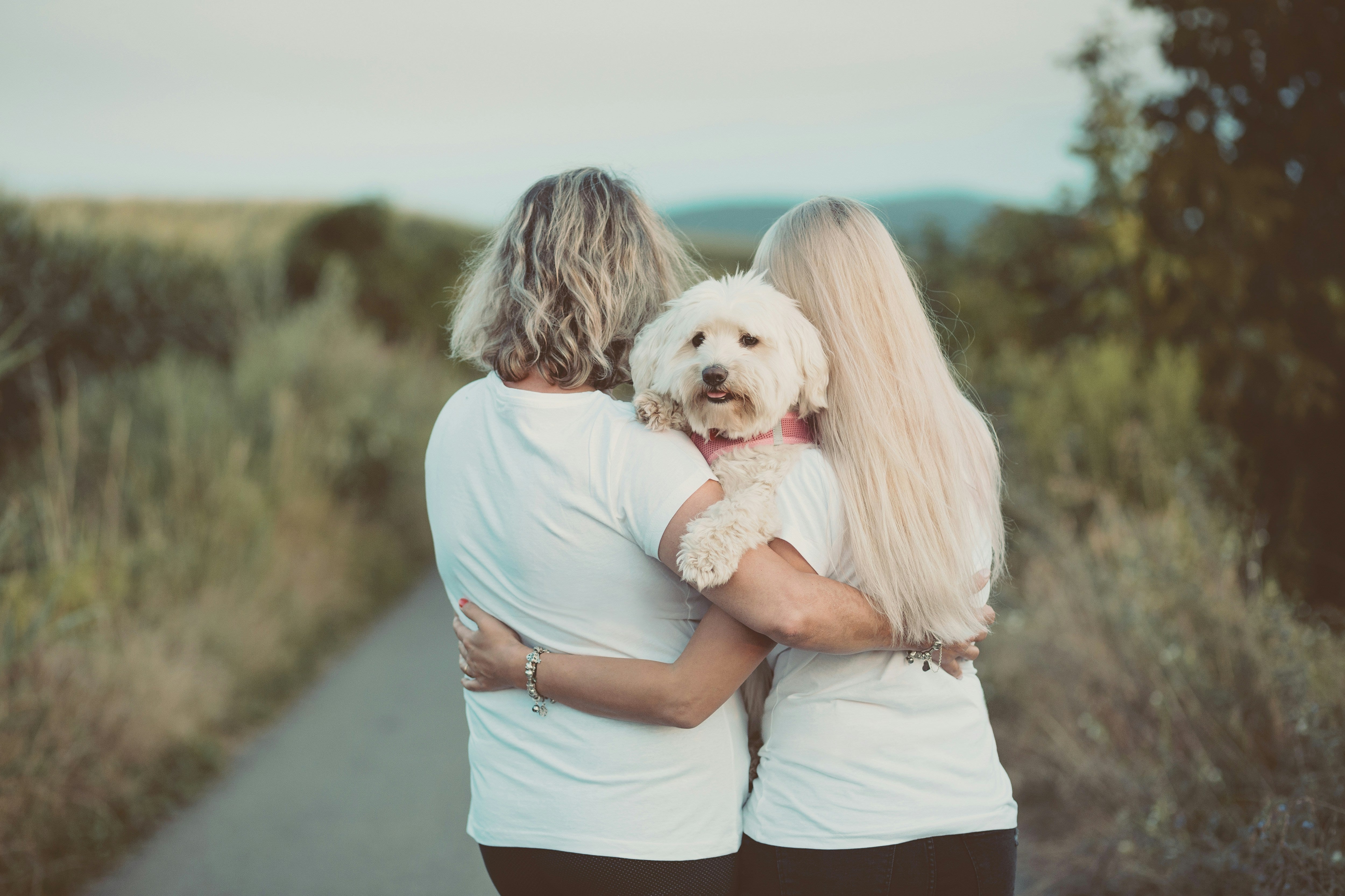 mother and daughter hugging on a lane with a white dog in their arms