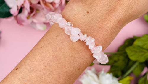 Woman's arm with healing crystal bracelet, the background I pale pink with floral decorations