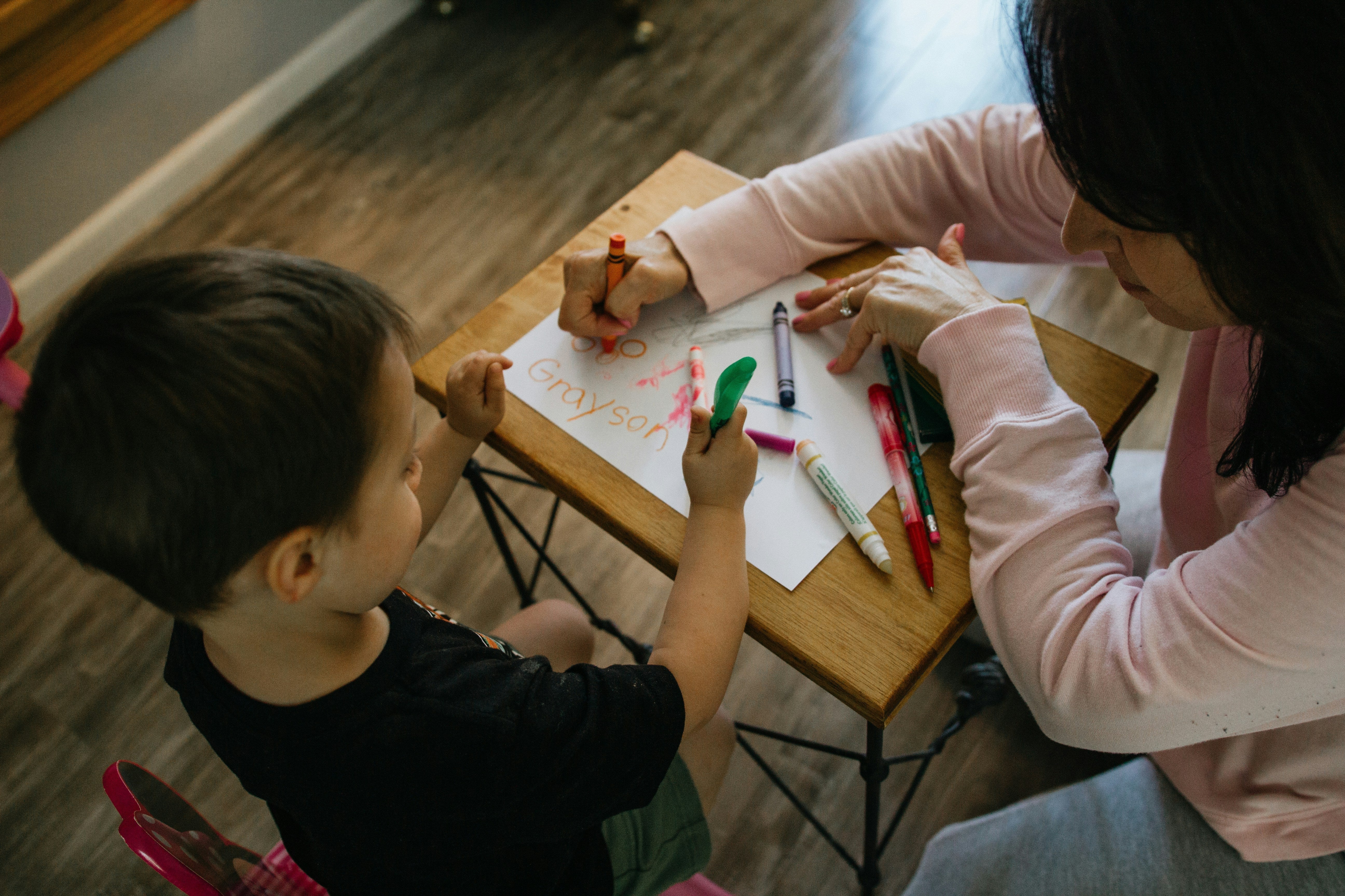 A teacher helping a child writing at a desk. Gifts to thank teachers.