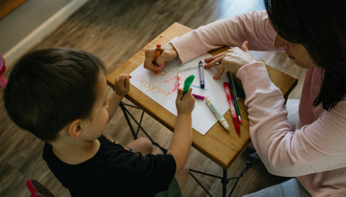 A teacher helping a child writing at a desk. Gifts to thank teachers.