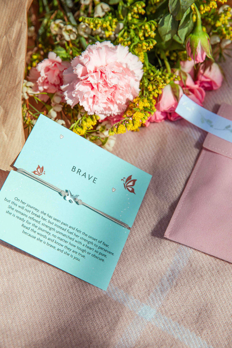 A pink blanket, velvet pouch and flowers. With a 'brave' gift to encourage someone when heading into a new chapter or back to school. The bracelet is a grey cord with a dainty butterfly charm