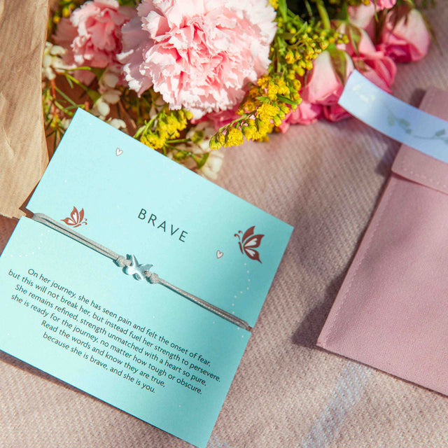 A pink blanket, velvet pouch and flowers. With a 'brave' gift to encourage someone when heading into a new chapter or back to school. The bracelet is a grey cord with a dainty butterfly charm