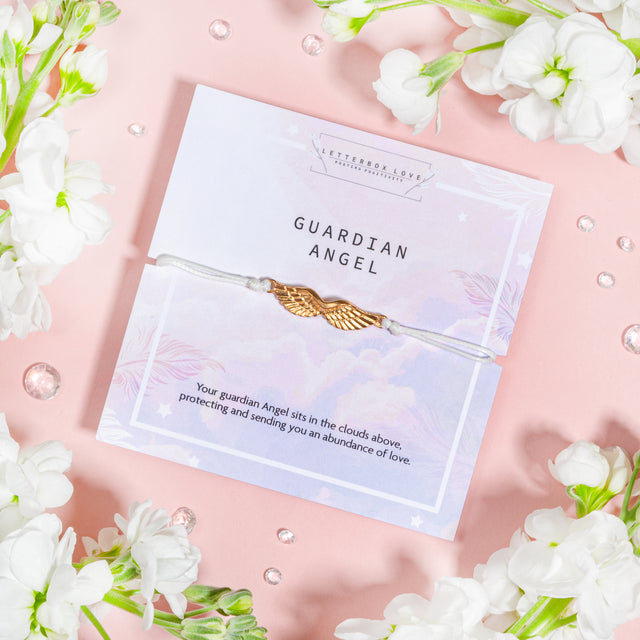Letterbox Love's 'Guardian Angel' bracelet with delicate gold angel wings on a light cord, accompanied by a heartfelt message about protection and love on a pastel cloud-themed background.