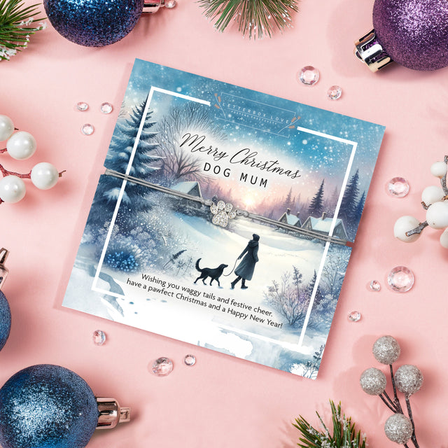 Letterbox Love Merry Christmas Dog Mum bracelet with a pawprint charm, perfect stocking filler or Secret Santa gift for dog lovers. Set on a festive winter scene with Christmas baubles, pearls, and decorative items on a pink background.