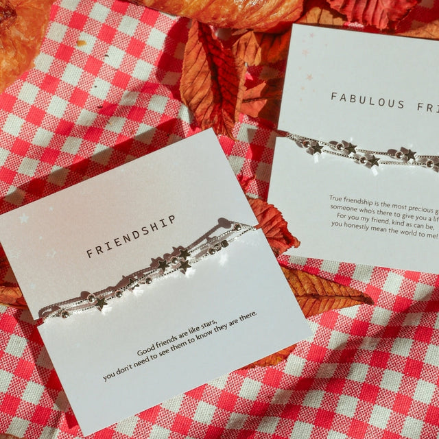 a checkered blanket with autumn leaves and two friendship gifts. a 'friendship' bracelet and a 'fabulous friend' with silver stars bracelets