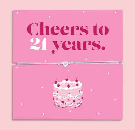 Pink 21st birthday gift card with the text “Cheers to 21 years” in bold pink and white lettering, featuring a silver and grey adjustable heart charm bracelet across the centre and an illustrated birthday cake underneath.
