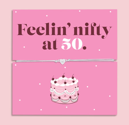 Pink 50th birthday gift card with the text “Feelin’ nifty at 50” in bold brown and white lettering, featuring a silver and grey adjustable heart charm bracelet across the centre and an illustrated birthday cake below.