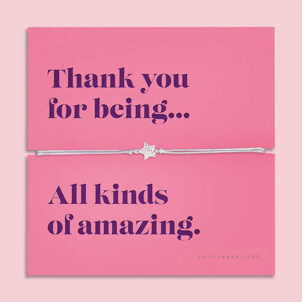 A silver-plated star charm bracelet on a soft, adjustable cord, displayed on a vibrant pink backing card with the message: "Thank you for being… All kinds of amazing." Surrounded by delicate purple flowers on a soft pink background. Perfect for gifting.