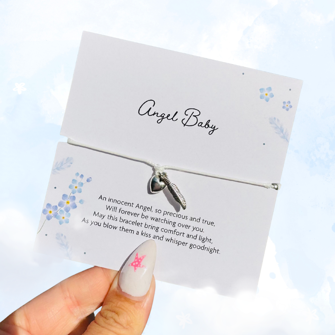 A hand with a glittery nail design holds a white card containing a delicate silver heart & feather charm on a thin string, with a poem printed on the front. The background is a soft, cloudy sky blue.