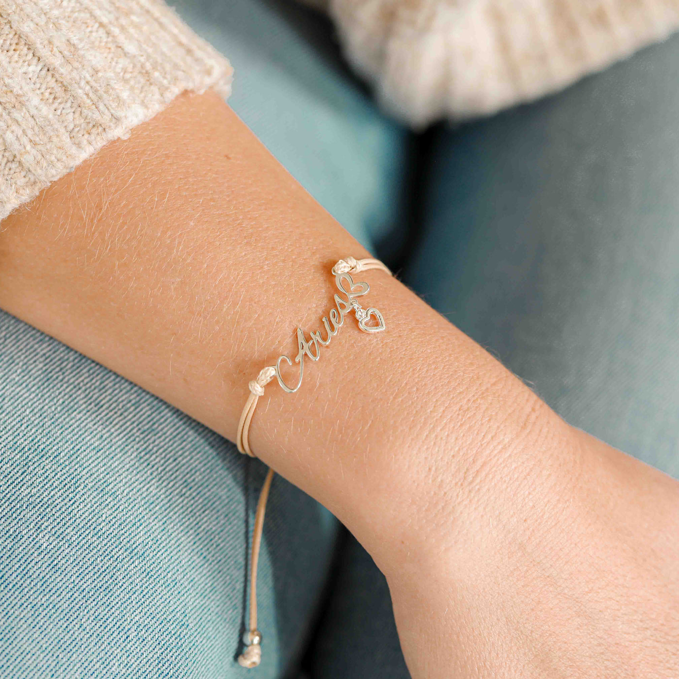 A woman wearing a dainty bracelet with the word “Aries” and a small heart charm, a lovely zodiac-inspired gift for her.