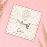 Aries-themed bracelet on a branded card with decorative elements on a pink background. Zodiac jewellery for women.