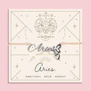 Peach cord bracelet featuring a silver 'Aries' script charm with heart pendant, presented on a zodiac card with ram illustration and personality traits "Ambitious, Bold, Honest".