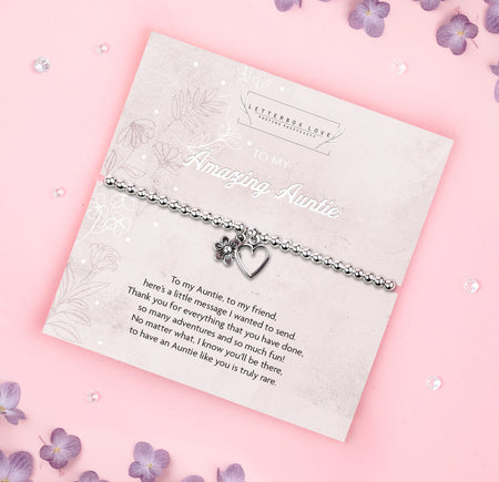 A silver beaded bracelet with a heart and flower charm displayed on a card reading 