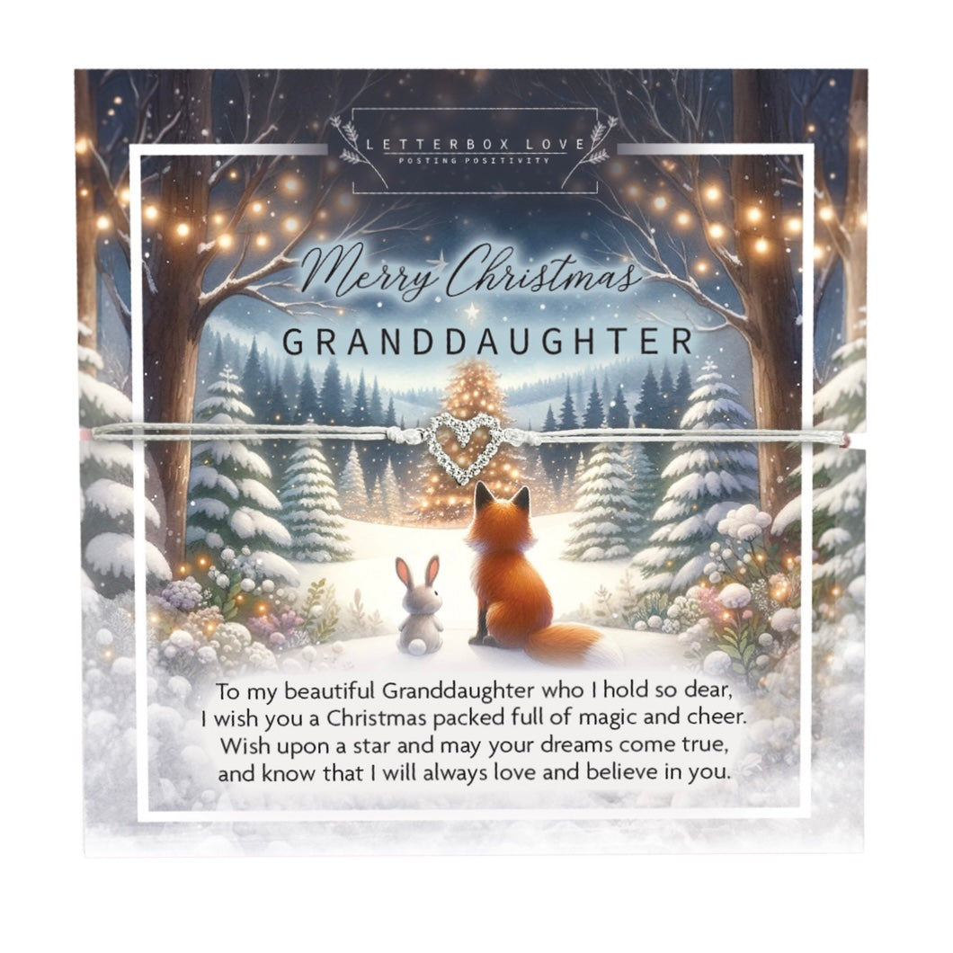 A delicate Christmas bracelet designed for a granddaughter, featuring a sparkling heart charm on a thin white cord. The bracelet is displayed on a festive card with a charming winter scene, depicting a fox and a rabbit sitting together in a snowy forest under twinkling fairy lights. The card includes the message: 