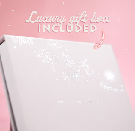 A pale pink background with text that reads 'luxury gift box included' and an arrow pointing to the box. The box is white with floral silver details.