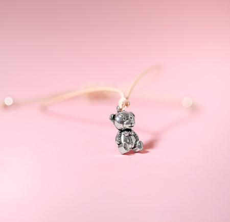 Pink background with a string bracelet with a cute little silver bear charm