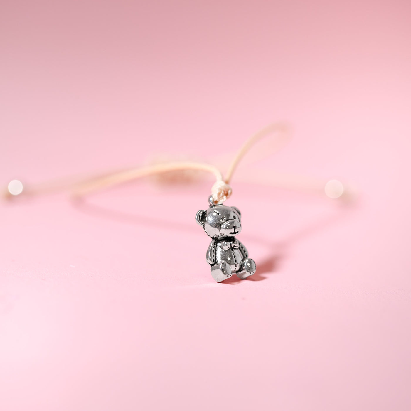 Pink background with a string bracelet with a cute little silver bear charm