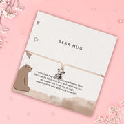 Card with a bear hug charm and text on a pink background