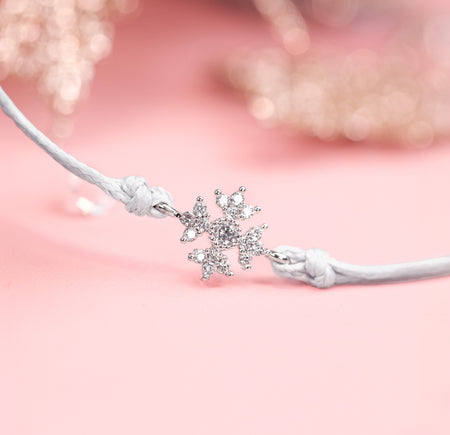Silver snowflake charm on a white friendship bracelet against a pink background. A beautiful bracelet for a Secret Santa gift.
