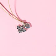 pale pink background with beige string bracelet with bee and heart charms