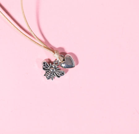 pale pink background with beige string bracelet with bee and heart charms