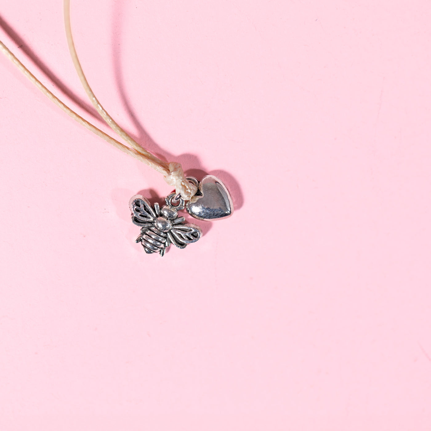 pale pink background with beige string bracelet with bee and heart charms