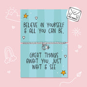 A silver charm bracelet displayed on a light blue striped card that reads 'BELIEVE IN YOURSELF & ALL YOU CAN BE, GREAT THINGS AWAIT YOU, JUST WAIT & SEE'. The card is set against a pink background with cute white doodles, and a 'MINI MOMENTS' brand sticker is shown in the top right corner.