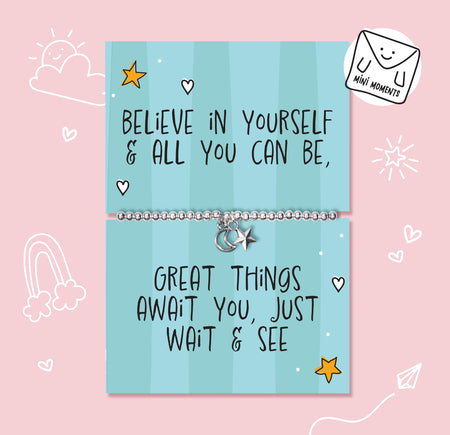 A silver charm bracelet displayed on a light blue striped card that reads 'BELIEVE IN YOURSELF & ALL YOU CAN BE, GREAT THINGS AWAIT YOU, JUST WAIT & SEE'. The card is set against a pink background with cute white doodles, and a 'MINI MOMENTS' brand sticker is shown in the top right corner.