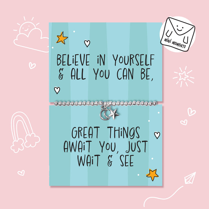 A silver charm bracelet displayed on a light blue striped card that reads 'BELIEVE IN YOURSELF & ALL YOU CAN BE, GREAT THINGS AWAIT YOU, JUST WAIT & SEE'. The card is set against a pink background with cute white doodles, and a 'MINI MOMENTS' brand sticker is shown in the top right corner.