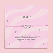 A pink bracelet card with two heart charms, featuring the text "Bestie" and a heartfelt poem expressing friendship. The bracelet is adjustable with a light pink cord, symbolizing the bond between best friends.
