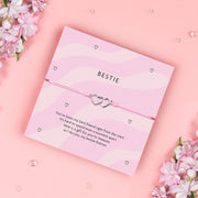 A pink bracelet card with two heart charms, featuring the text "Bestie" and a heartfelt poem expressing friendship. The bracelet is adjustable with a light pink cord, symbolizing the bond between best friends.