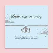 Grey adjustable cord bracelet featuring silver plated cloud and heart charms on a keepsake card reading "Better Days Are Coming." A thoughtful encouragement, thinking of you, sympathy or cheer up gift, presented in a luxury white butterfly envelope.
