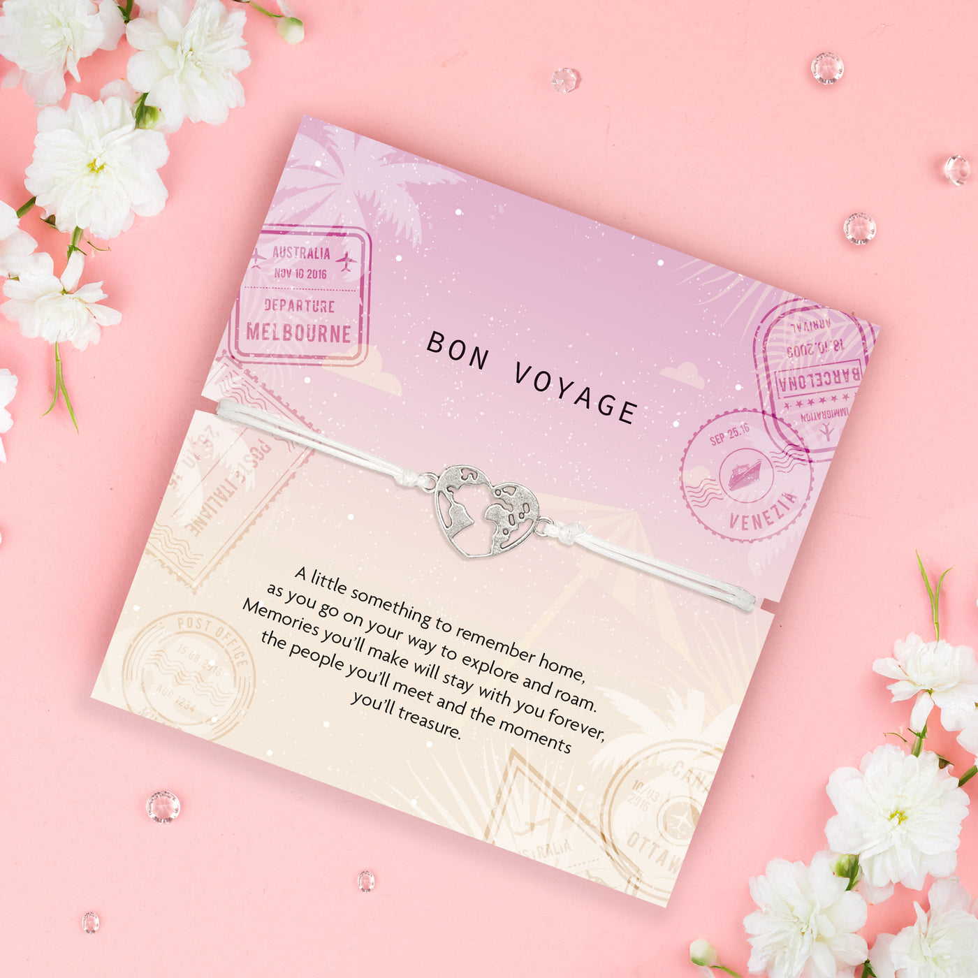 Bon Voyage card with a globe and heart charm on a pink background with white flowers. An affordable travel gift for her
