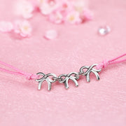 A close-up image of a cute friendship bracelet with pink cord and three small silver-plated bows, creating a perfect gift for a friend