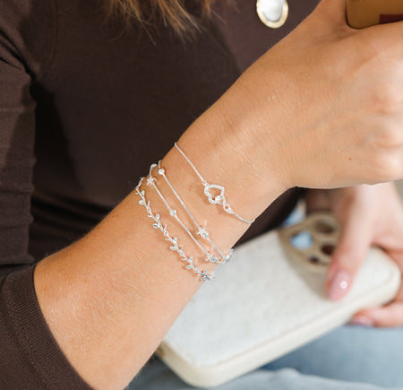 Person wearing multiple silver bracelets on wrist, holding a drink.