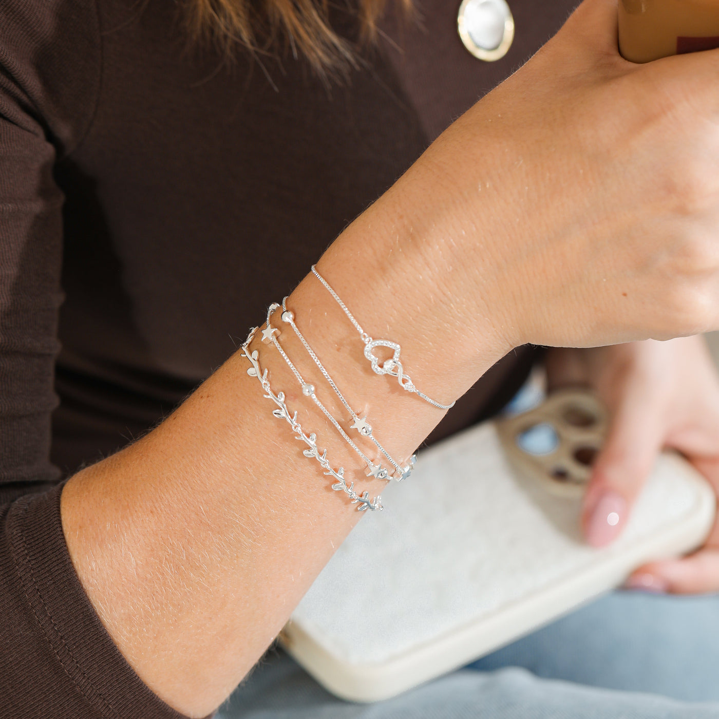 Person wearing multiple silver bracelets on wrist, holding a drink.