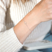A woman's wrist with an elegant silver heart bracelet, against a neutral background