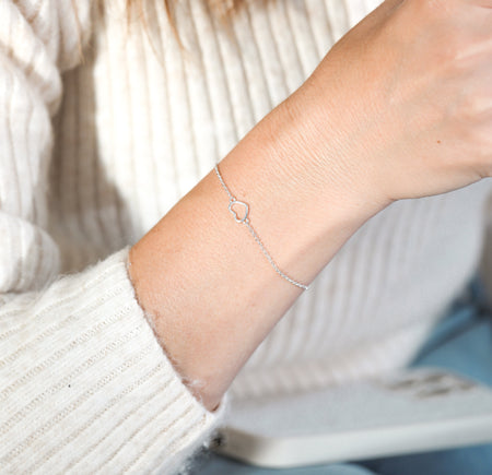 A woman's wrist with an elegant silver heart bracelet, against a neutral background