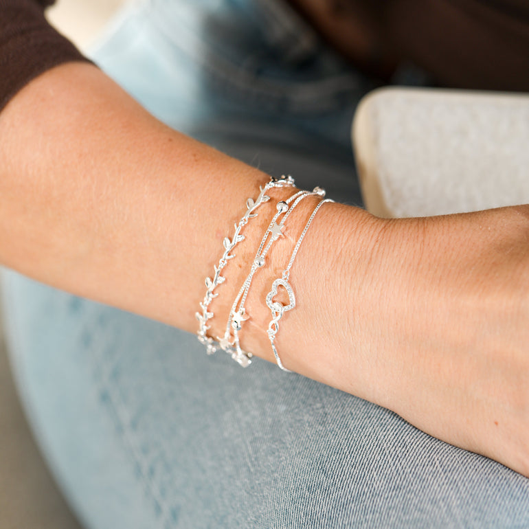Close-up of a wrist wearing multiple silver bracelets on a blurred background