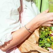 Person holding a matcha and a bouquet of flowers against a green background, she is wearing a silver plated beaded star bracelet