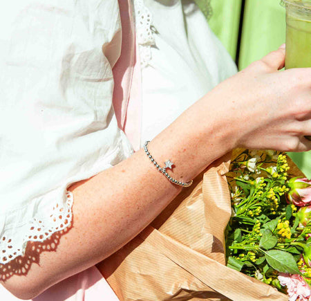 Person holding a matcha and a bouquet of flowers against a green background, she is wearing a silver plated beaded star bracelet