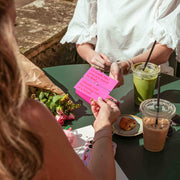 Two people sitting at a table outdoors with drinks and food.
